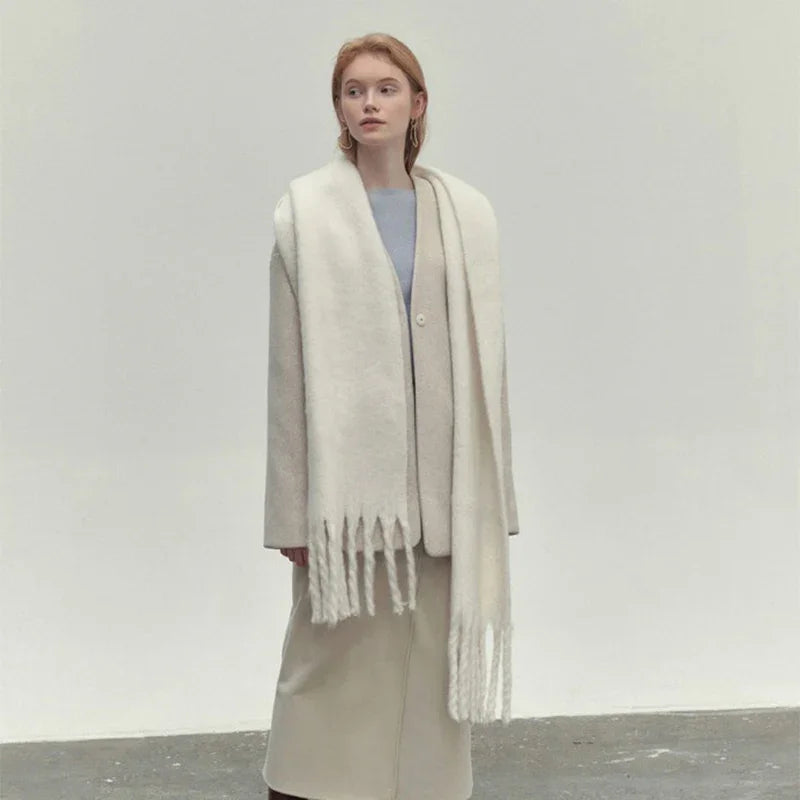 Woman wearing beige coat and long white fringed scarf against plain background