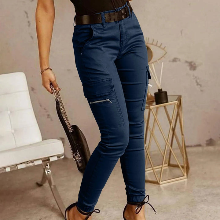 Woman wearing navy blue cargo pants with zipper pockets and ankle ties, holding black handbag chain