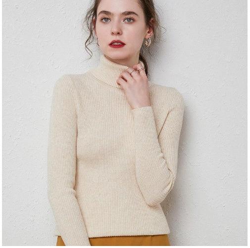 Young woman wearing a beige ribbed turtleneck sweater against a white textured wall