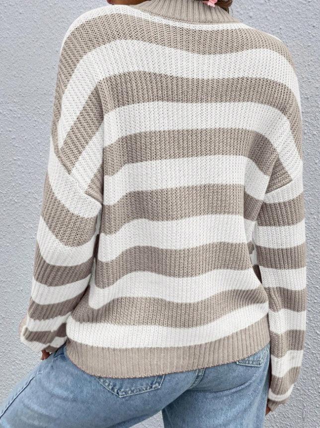 Back view of person wearing beige and white striped chunky knit sweater paired with light blue jeans against gray wall