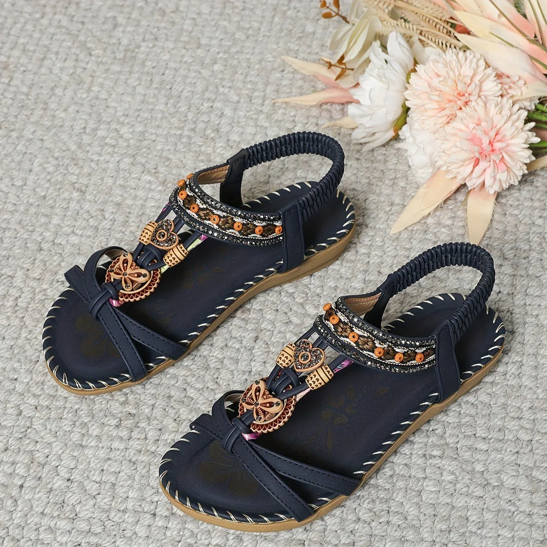Navy blue women’s sandals with decorative wooden beads and elastic back straps on grey carpet