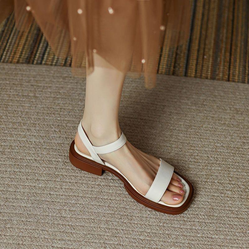 Close-up of foot wearing white leather open-toe sandal with brown sole on textured carpet