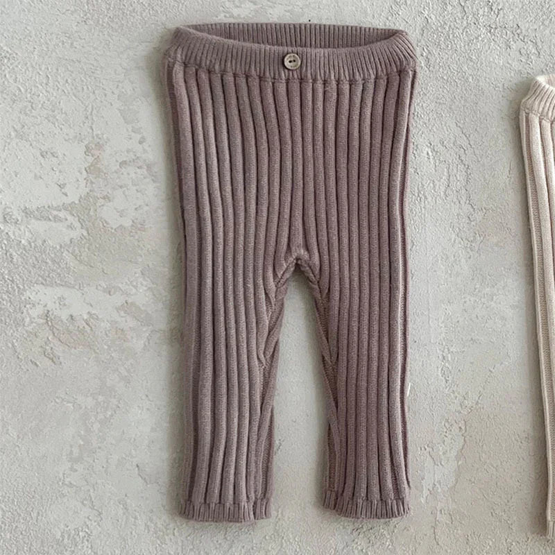 Ribbed knit baby pants in dusty pink with a button on elastic waistband against textured wall