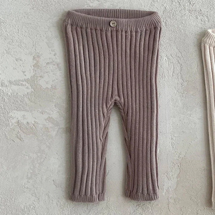 Ribbed knit baby pants in dusty pink with a button on elastic waistband against textured wall