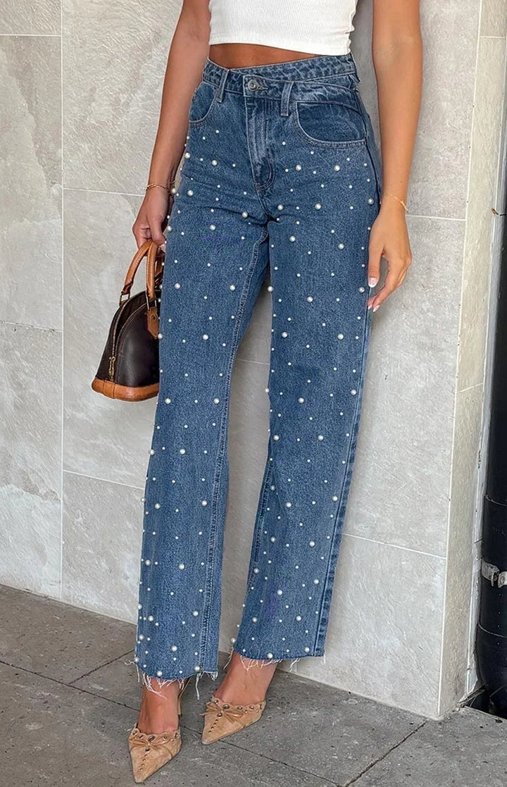 Woman wearing high-waisted blue jeans with pearl embellishments and frayed hems, paired with tan pointed heels and a brown handbag