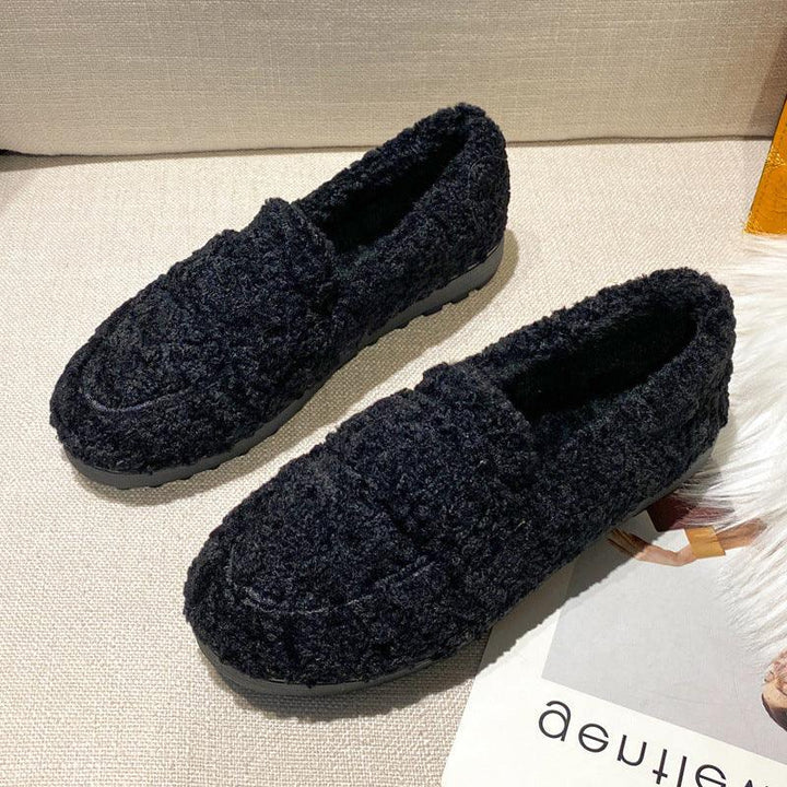 Pair of black textured fuzzy slip-on loafers with rubber soles on beige fabric surface