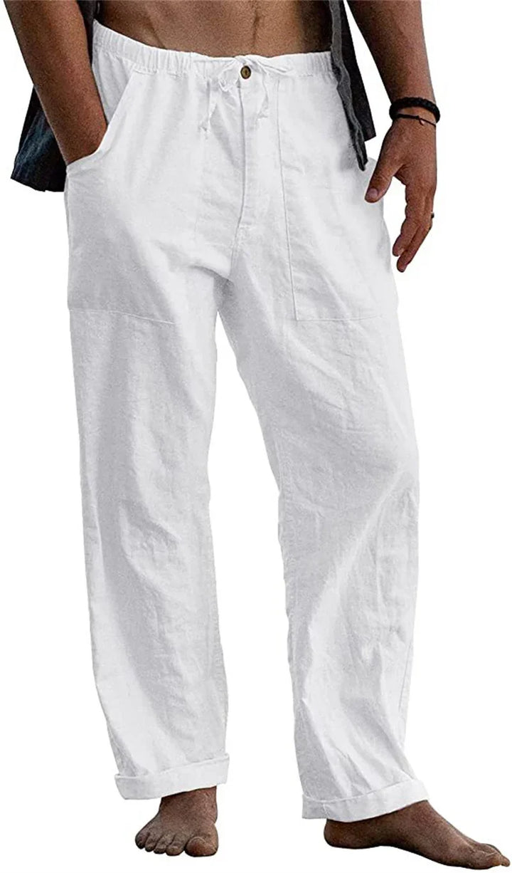 Male model wearing loose white linen pants with drawstring waist and rolled cuffs barefoot