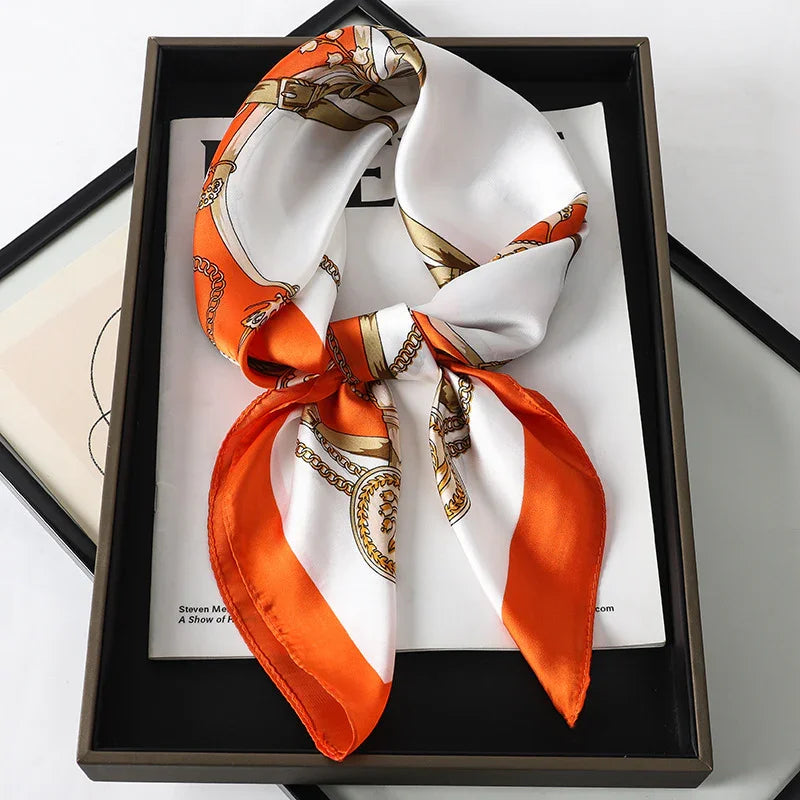 Elegant silk scarf with orange and white pattern featuring gold chains, displayed in black box