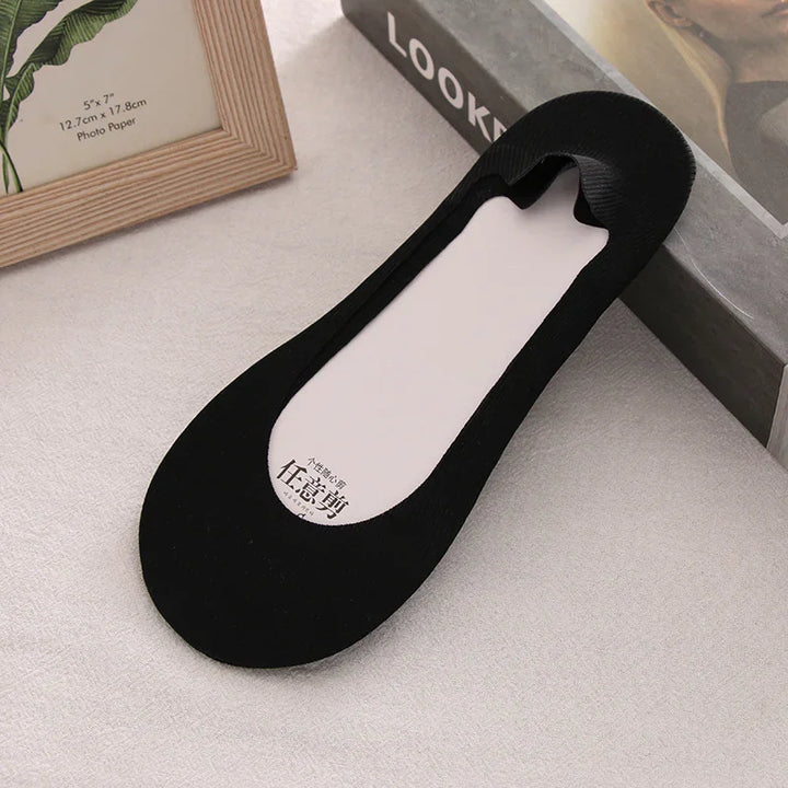 Black no-show sock liner on a gray surface next to photo frame and art book