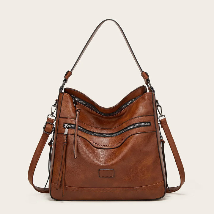 Brown leather shoulder handbag with front zipper pocket and adjustable straps on beige background