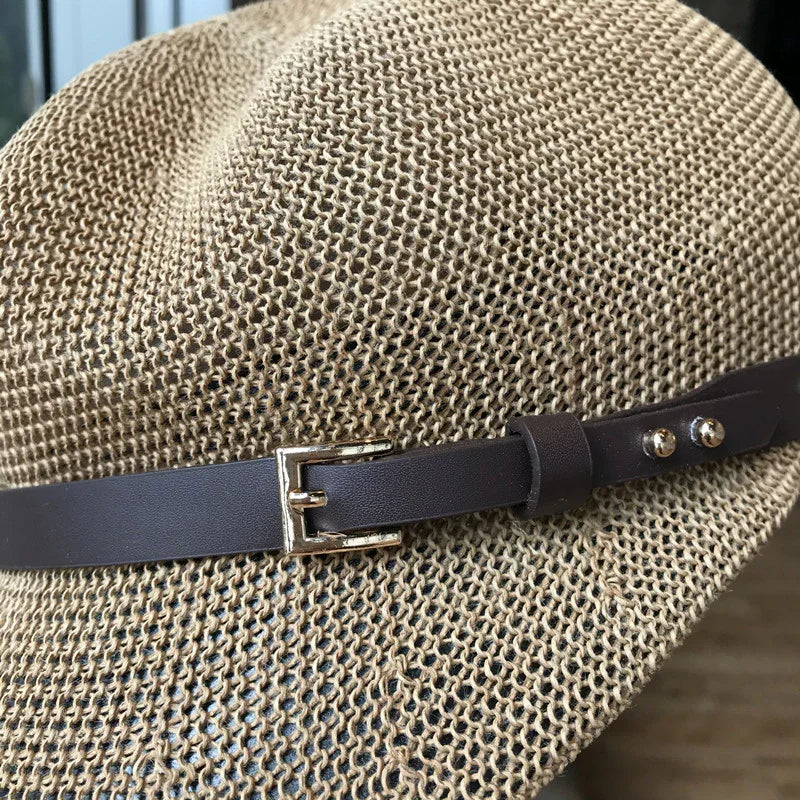 Close-up of woven beige straw hat with dark brown leather belt and silver buckle detail