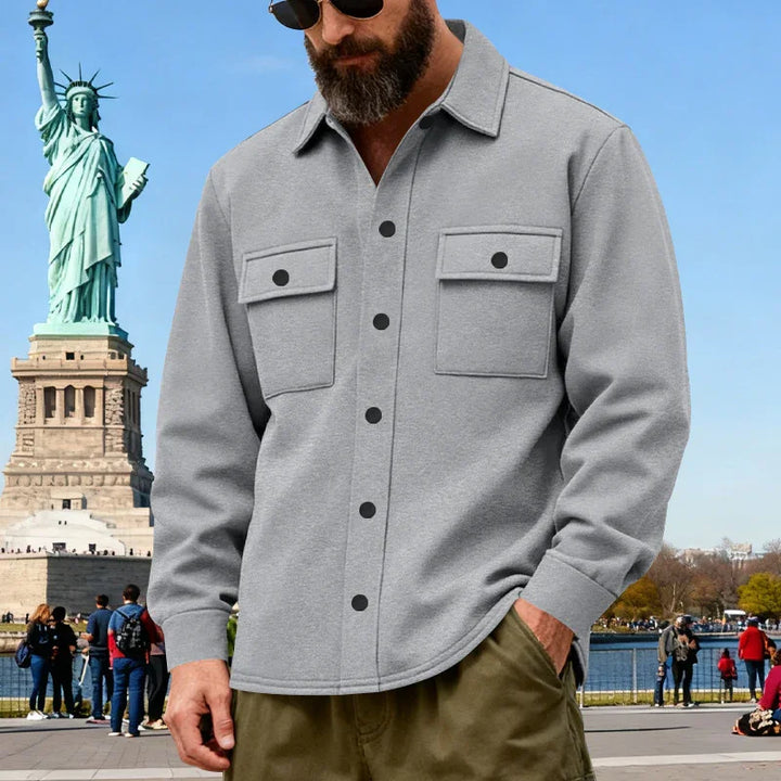 Man wearing gray button-up shirt with chest pockets near Statue of Liberty on a sunny day