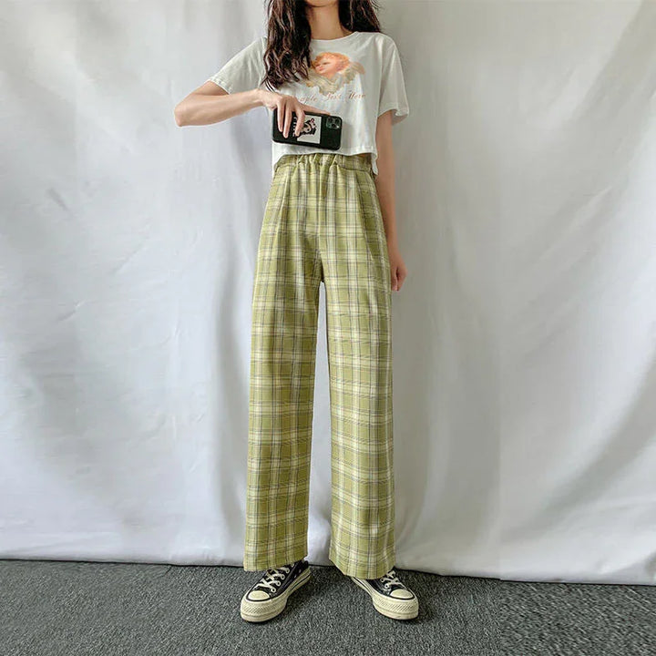 Woman wearing green plaid wide-leg pants, graphic cropped tee, and black sneakers, holding smartphone