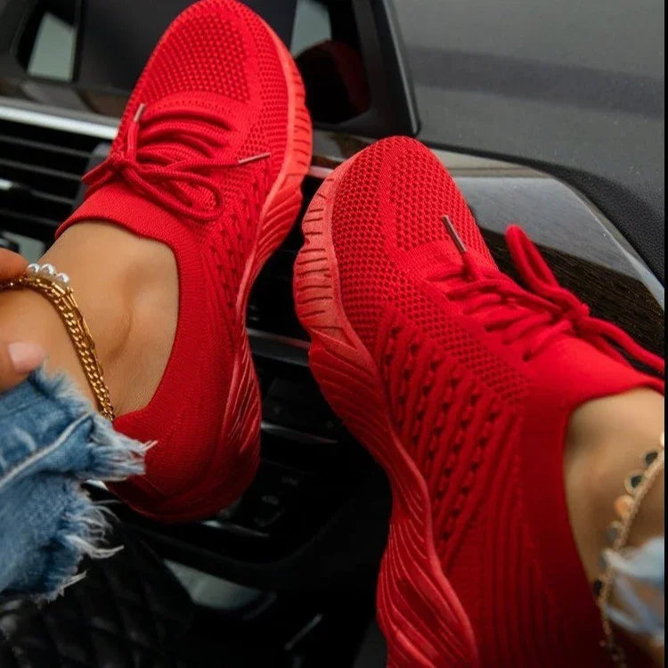 Close-up of red knit sneakers worn with ankle bracelets inside a car interior