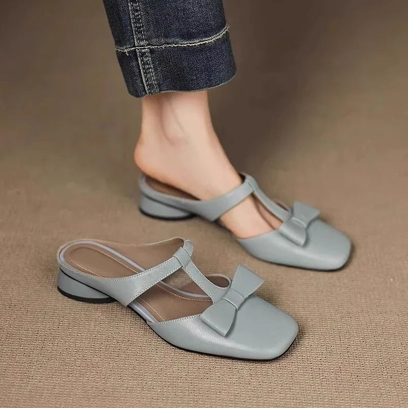 Light gray leather low heel mules with T-strap and bow detail worn with cuffed denim jeans
