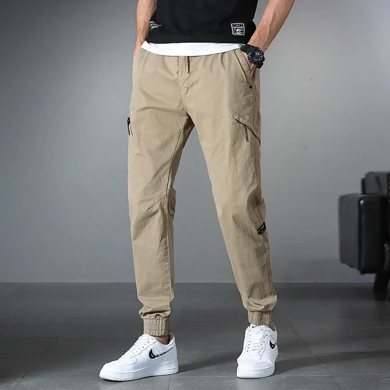Men's beige cargo jogger pants with elastic cuffs paired with white Nike sneakers indoors