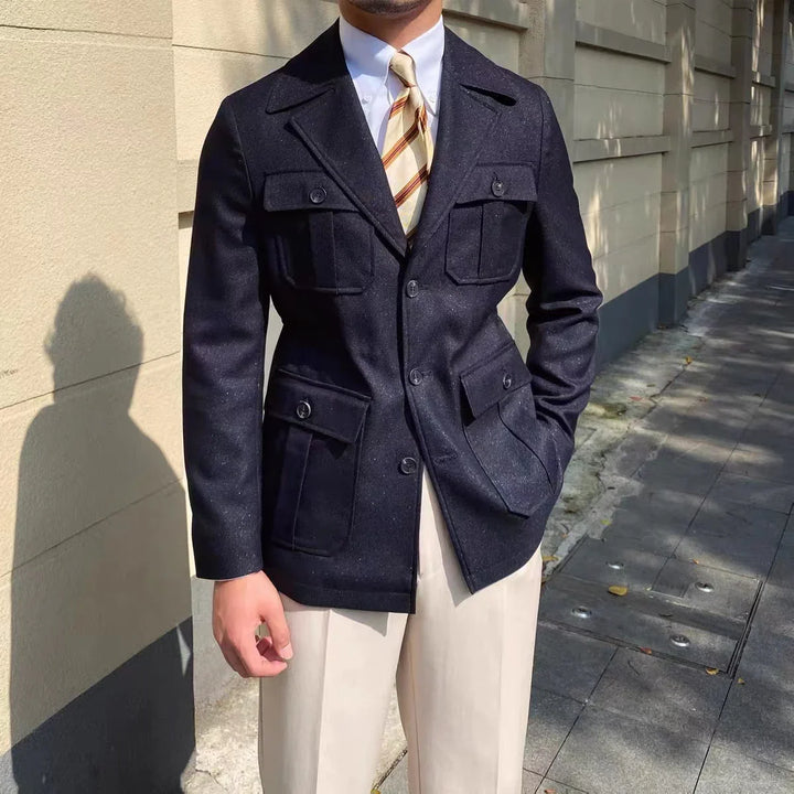 Man wearing navy blue buttoned jacket with flap pockets and beige trousers outdoors