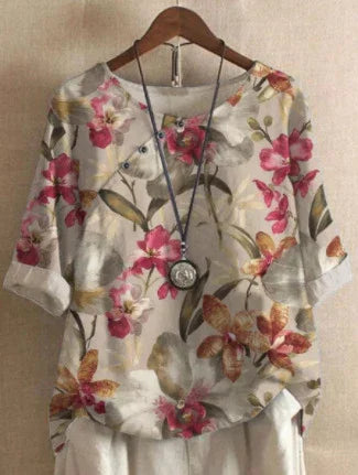 Floral print blouse with pink and orange flowers, 3/4 sleeves, paired with white pants and a long pendant necklace