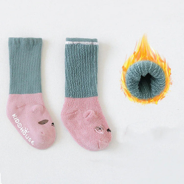 Pair of green and pink kids' warm socks with bear face design and flame indicating thermal insulation