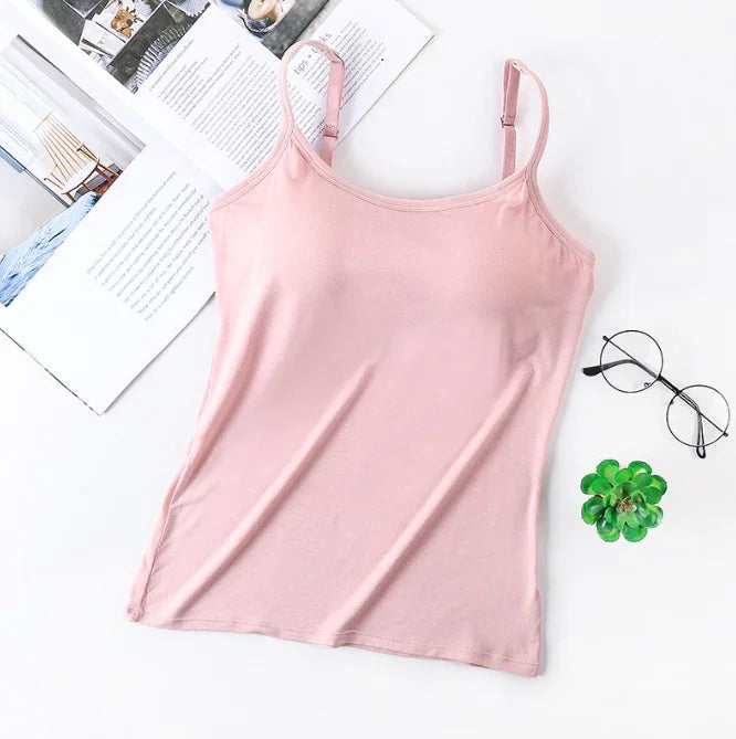Light pink spaghetti strap camisole top on white surface with open magazine, black round glasses, and small green succulent