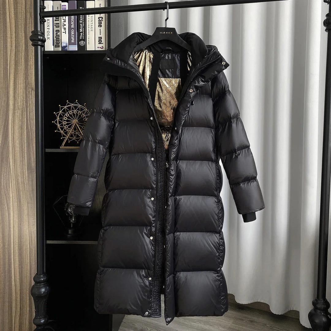 Long black puffer winter coat with shiny shell and gold patterned lining, hanging on rack