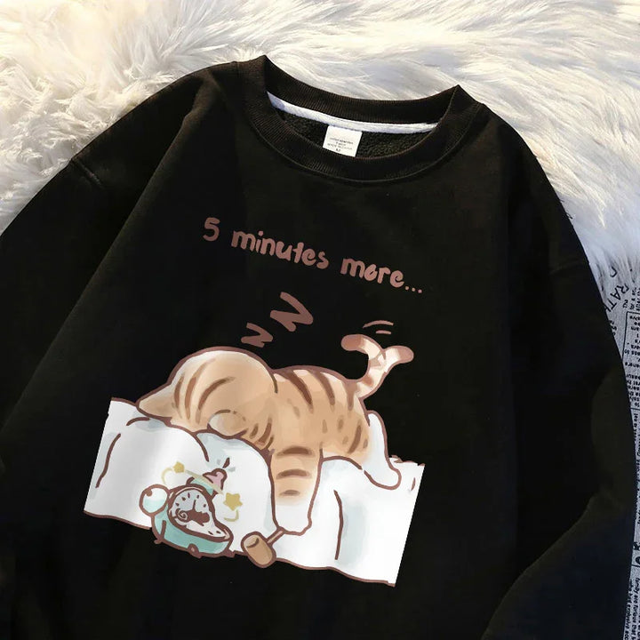 Black sweatshirt with cartoon sleeping cat and text '5 minutes more' on white blanket and old alarm clock