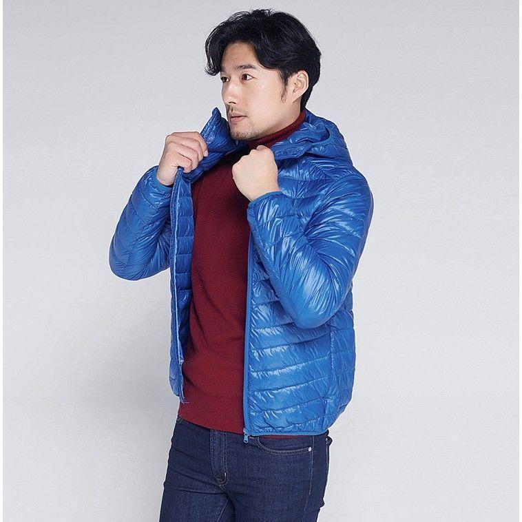 Man wearing blue quilted hooded jacket over red sweater and dark jeans against plain background