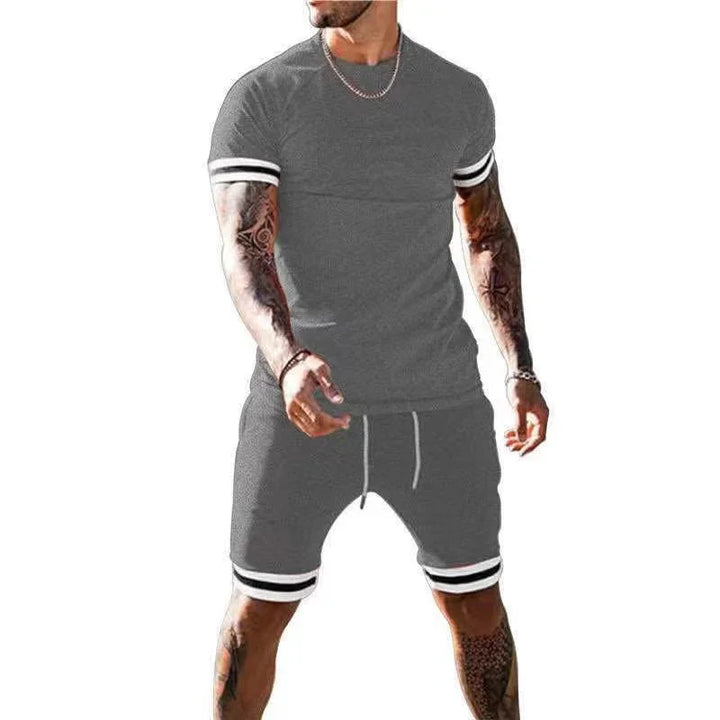 Man wearing gray athletic short sleeve shirt and shorts with white and black striped cuffs