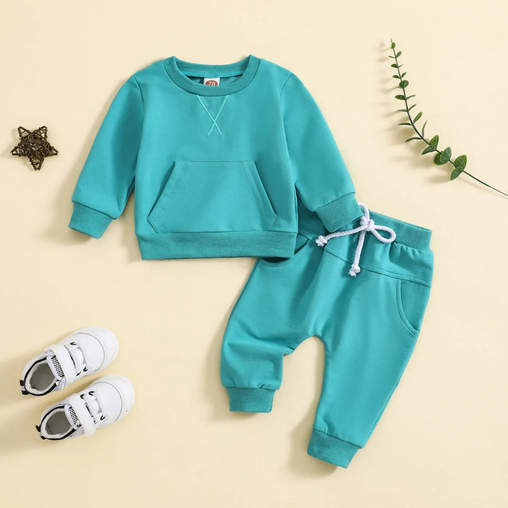 Turquoise baby toddler sweatshirt and pants set with white shoelaces and white sneakers on beige background