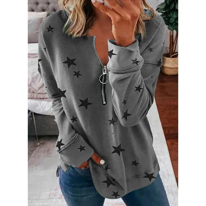 woman wearing gray long sleeve star print top with front zipper in cozy home setting