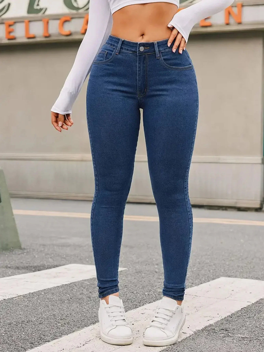 Woman wearing high-waisted blue skinny jeans and white sneakers on urban street