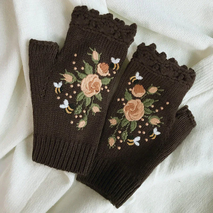 Brown fingerless knitted gloves with embroidered peach roses, green leaves, and white bees on white fabric background