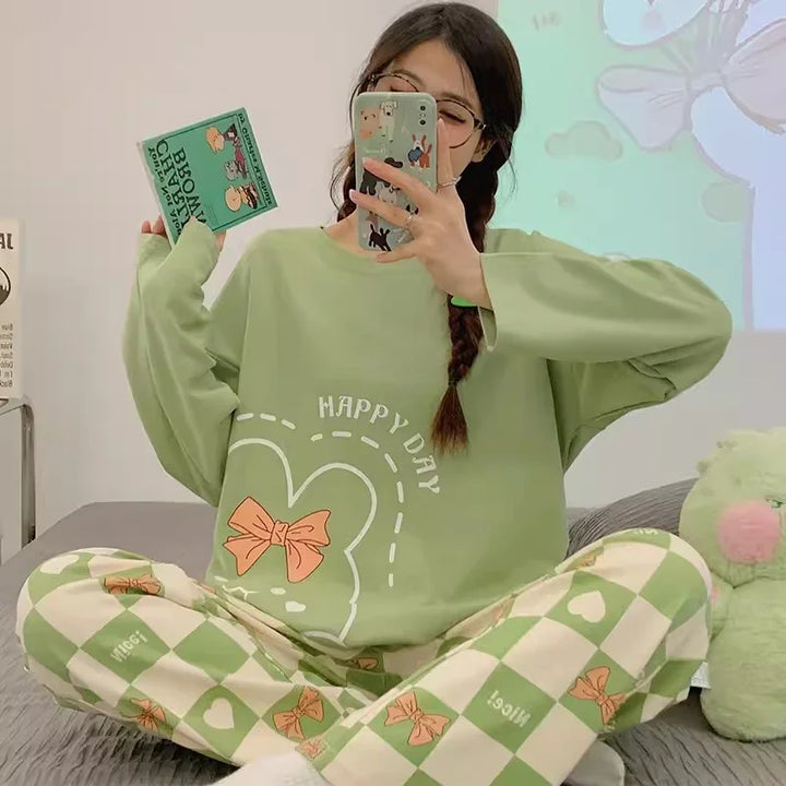 Woman in green happy day sweatshirt and checkered pajama pants with orange bows taking mirror selfie on bed