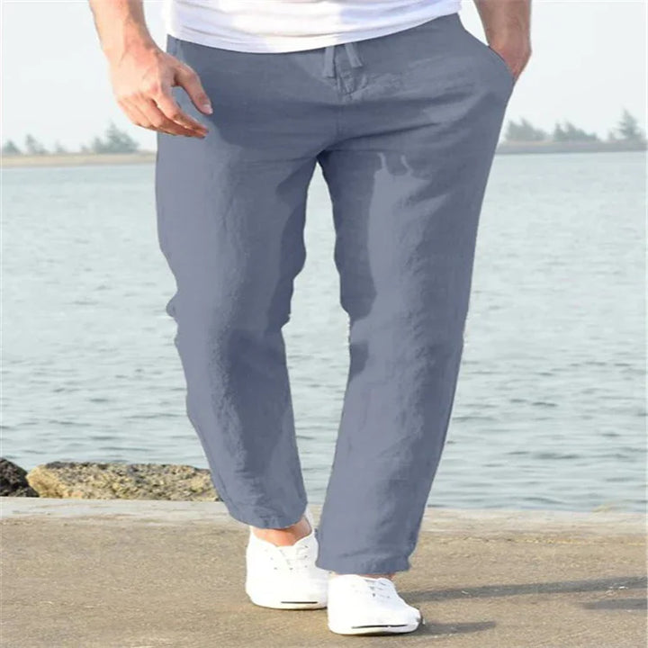 Man wearing gray casual pants and white sneakers walking near a waterfront on a sunny day