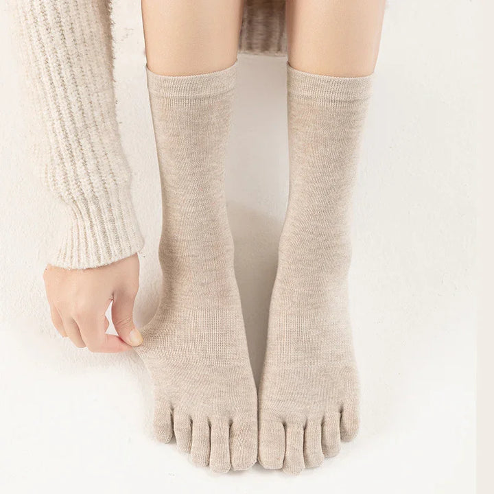 Close-up of beige toe socks on feet with a hand adjusting the fabric, wearing a cream knit sweater