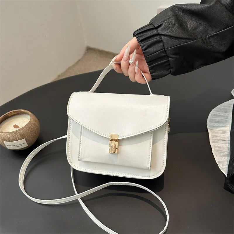 White leather handbag with gold clasp held by hand on black table with candle