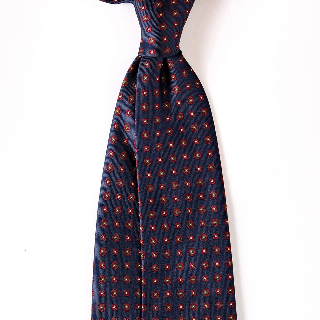Navy blue silk tie with red and gold geometric floral pattern on white background