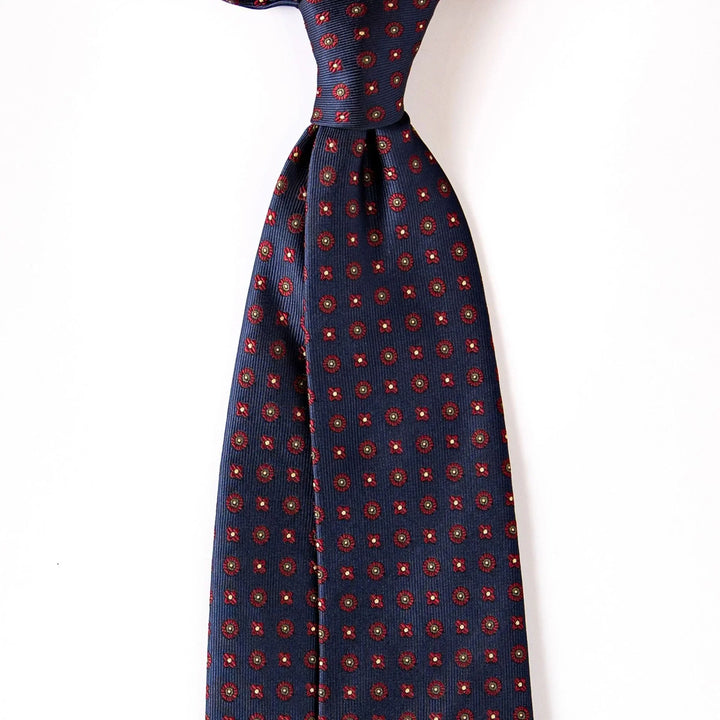 Navy blue silk tie with red and gold geometric floral pattern on white background