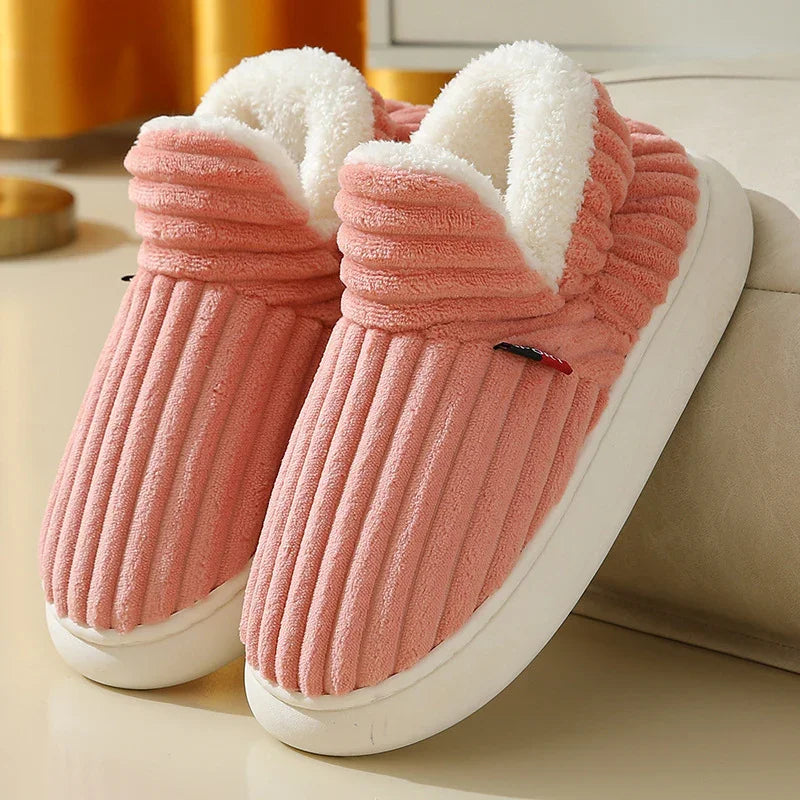 Pink plush indoor slippers with white fluffy lining and thick white soles on beige surface