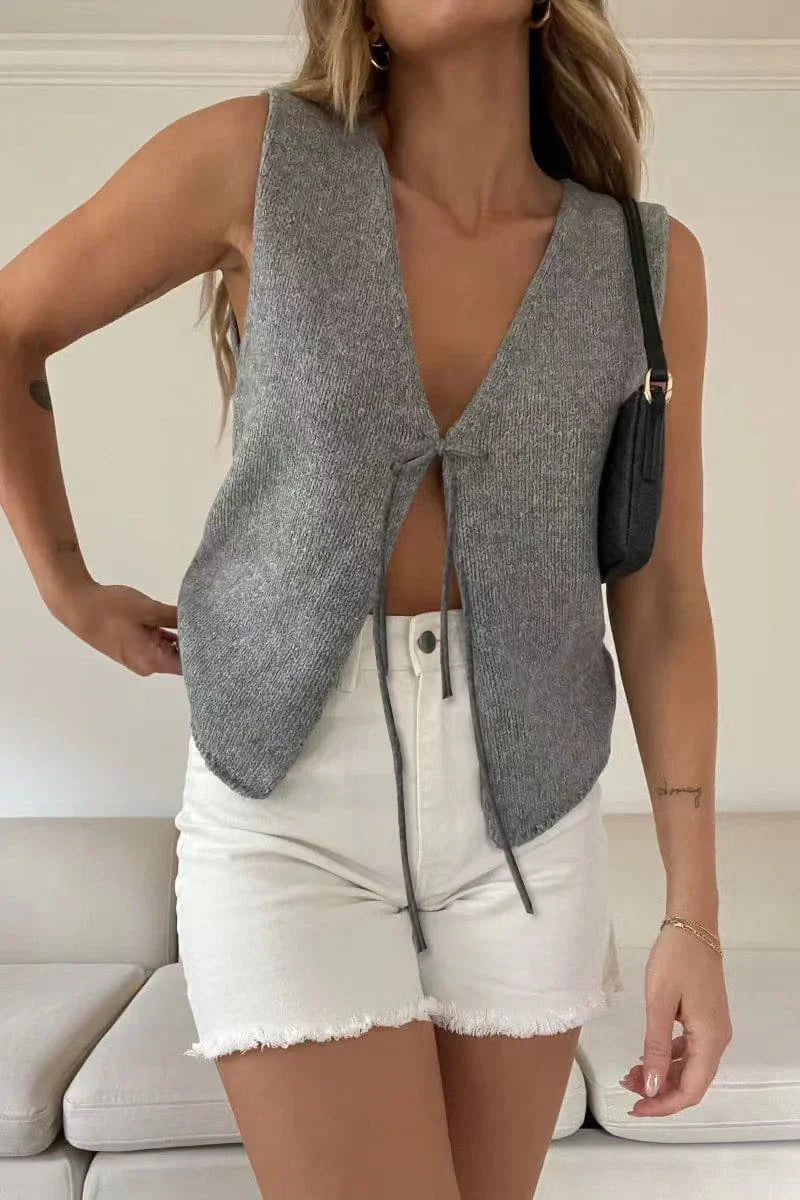 Woman wearing sleeveless gray knit vest with front tie and white frayed denim shorts indoors