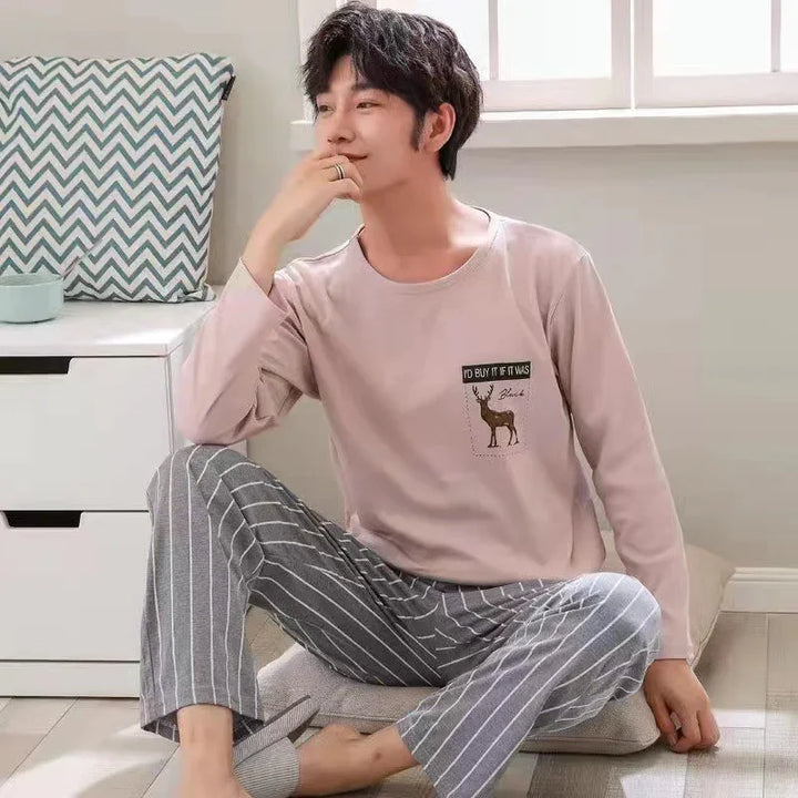 Man wearing beige long sleeve top with deer print and gray striped pajama pants sitting on floor cushion