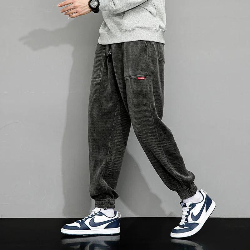 Man wearing dark gray corduroy jogger pants with elastic cuffs and blue white Nike sneakers