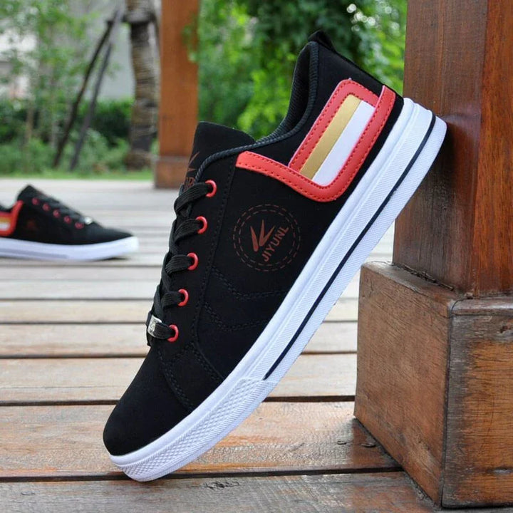 Black casual sneakers with red, white, and gold stripes resting against wooden post on deck