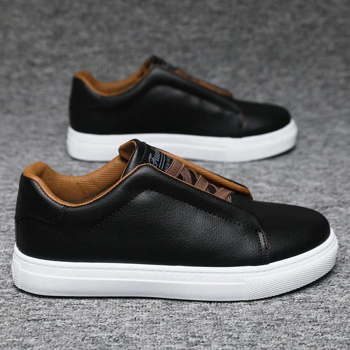 Black leather casual sneakers with brown inner lining and white rubber soles on gray carpet