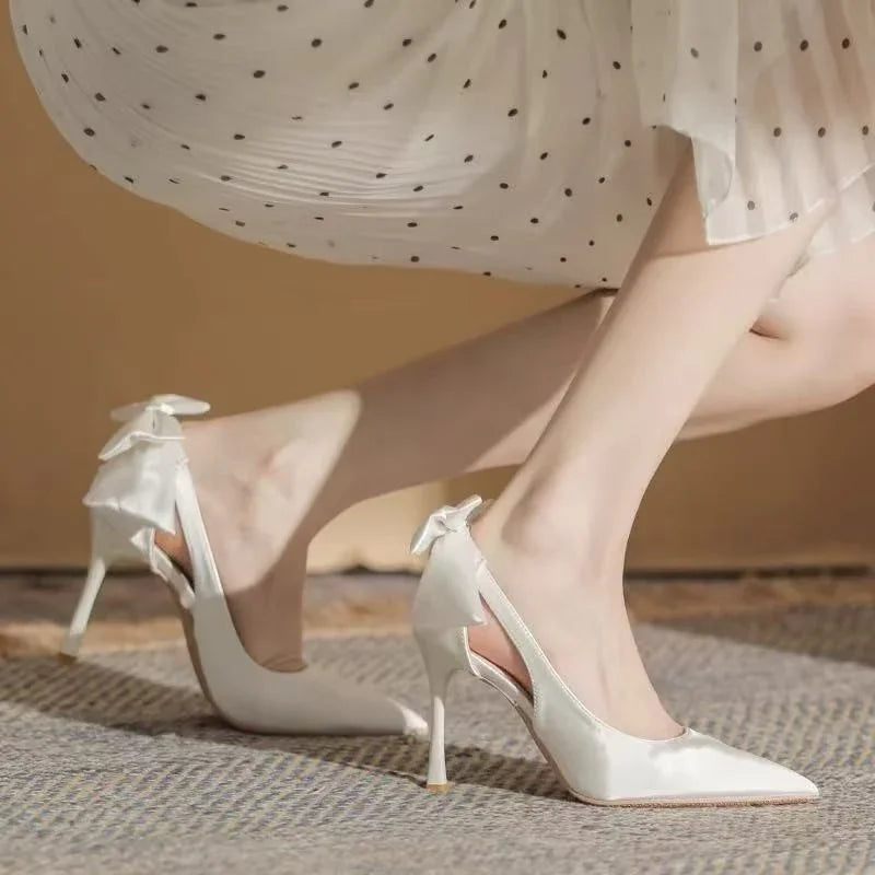 Close-up of elegant white high heel shoes with bow detail worn with a white polka dot dress