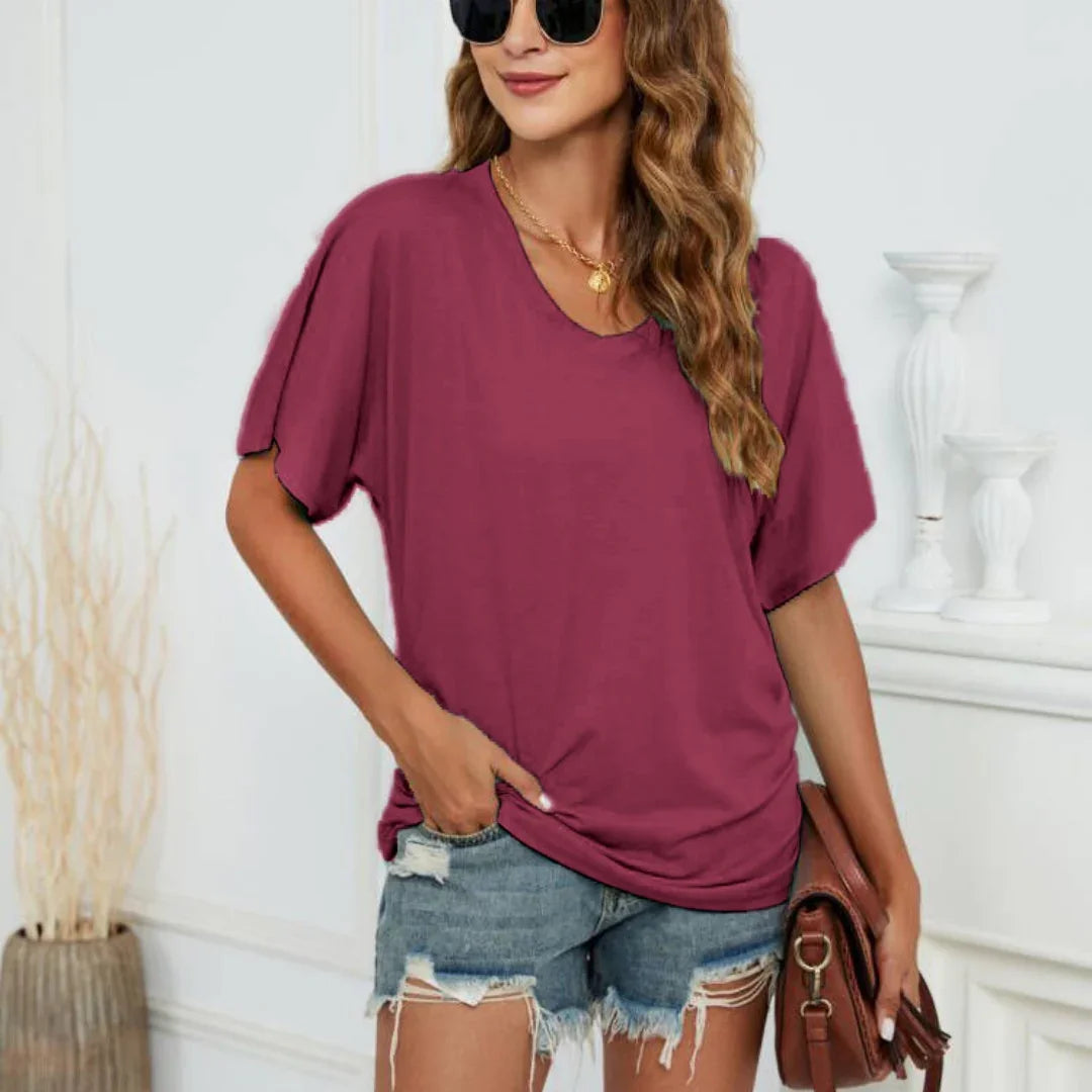 Woman wearing plum loose fit short sleeve top and distressed denim shorts, holding brown clutch