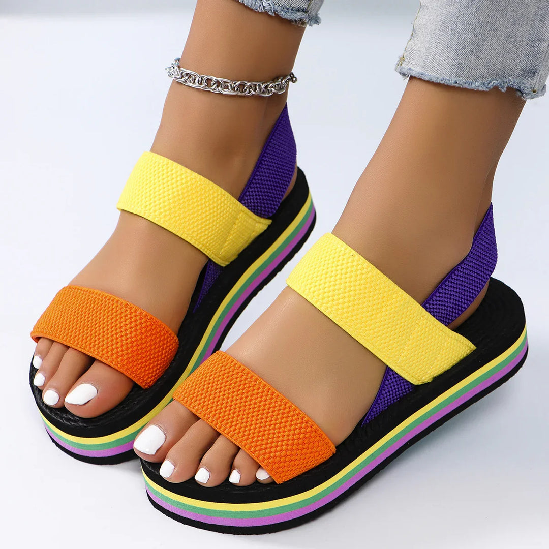 Colorful platform sandals with orange, yellow, and purple straps on feet with white nail polish