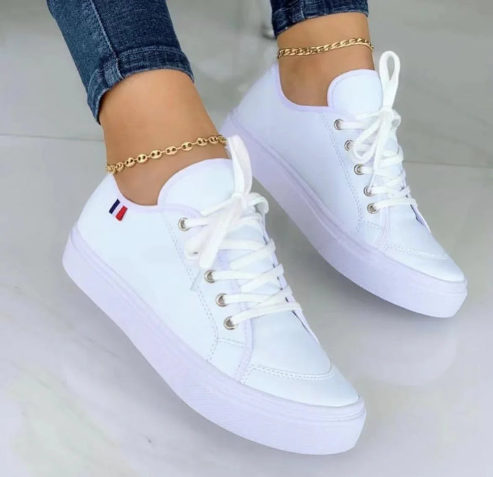 White platform sneakers with white laces worn with blue jeans and gold anklets on marble floor
