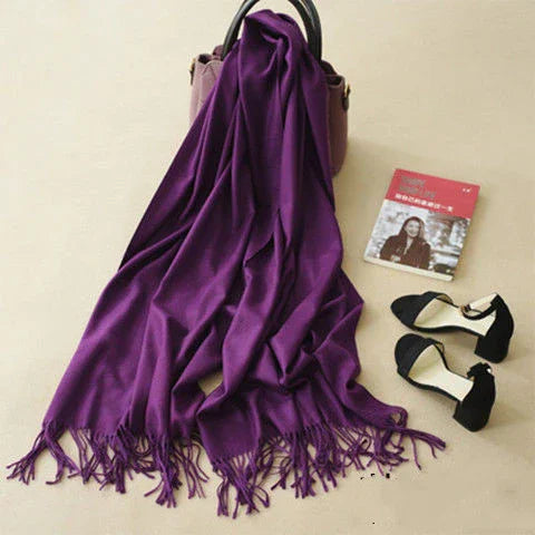 Purple fringe scarf draped over mauve handbag with black high heels and red book on beige background