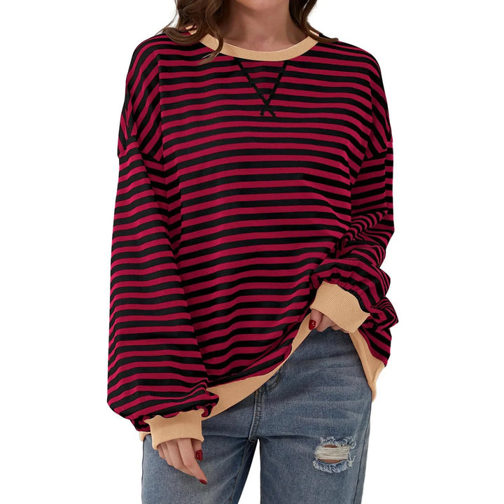 Woman wearing oversized red and black striped long sleeve sweater with beige cuffs and hem, paired with ripped jeans